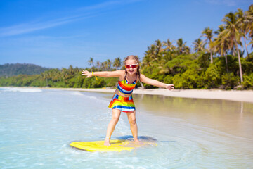 Child surfing on tropical beach. Surfer in ocean.