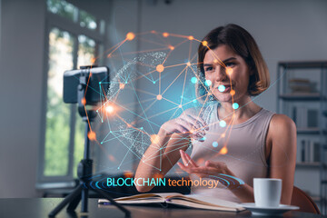 Happy woman is making video blog using smartphone on a tripod explaining with hands at office workplace. Concept of online stream, business education, conference call. Blockchain hologram