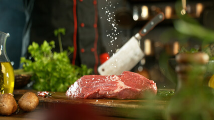 Close-up of falling salt on tasty beef steak in kitchen. Chef in background.