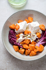 Plate with roasted sweet potato, radicchio, feta and chopped pistachios, vertical shot on a beige stone background, selective focus