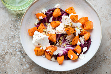 Plate with roasted sweet potato, feta cheese and radicchio salad, horizontal shot on a beige granite surface, high angle view