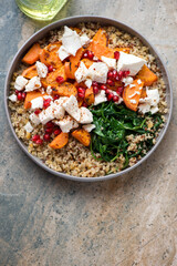 Quinoa with feta, roasted sweet potato, pomegranate and wilted spinach, vertical shot on a beige granite background, high angle view