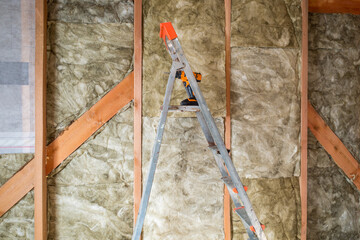 a folding metal staircase against the background of the wall of a frame house is insulated from the inside with mineral wool.