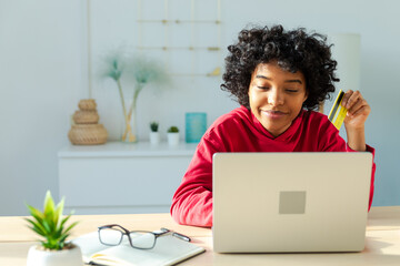 African american woman using laptop shopping online paying with gold credit card. Girl sitting at...