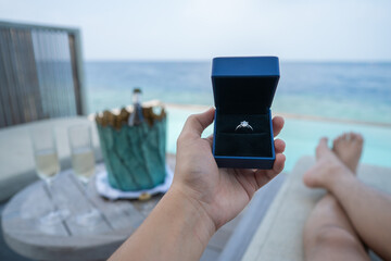 Hand holding a box with engagement ring with ocean view background.