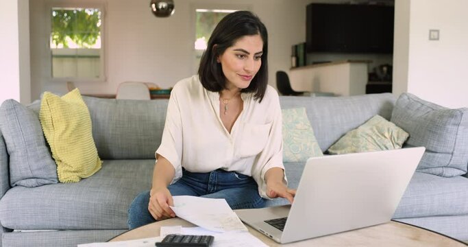 Focused Latina woman sit on sofa at home, pay bills via e-banking app using laptop, calculates incomes, control household expenses, planning, organizing. Family budgeting, finances management, savings