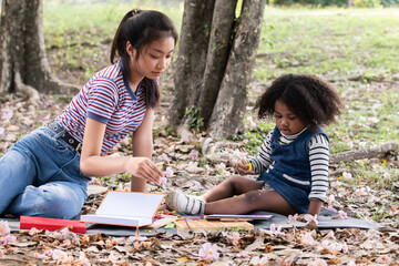 Adorable dark skinned and sister learning something together in the park. young mother and mixed race daughter playing game in garden.   enjoying while parents teach in garden.