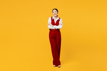 Full body cheerful young lawyer employee business woman of Asian ethnicity wear formal red vest shirt work at office hold hands crossed folded look camera isolated on plain yellow background studio.