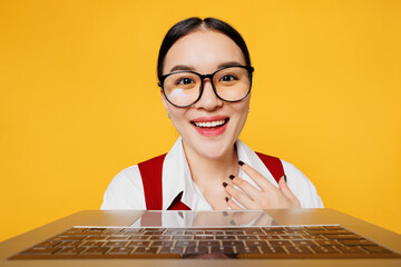 Young lawyer employee business woman of Asian ethnicity she wear formal red vest shirt glasses work at office typing on laptop pc computer keyboard isolated on plain yellow background. Career concept.
