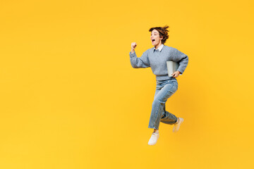 Fototapeta na wymiar Full body side view young IT woman wearing grey knitted sweater shirt casual clothes jump high hold run with laptop pc computer isolated on plain yellow background studio portrait. Lifestyle concept.