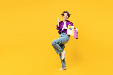 Full body young smiling woman wear casual purple shirt do housework tidy up hold basin with laundry clothes do winner gesture isolated on plain yellow background studio portrait. Housekeeping concept.