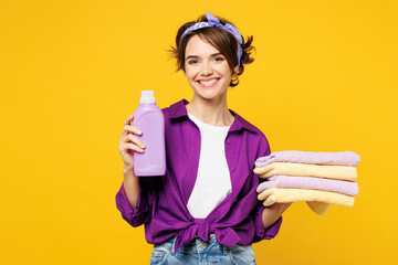 Young smiling happy satisfied woman she wear purple shirt do housework tidy up hold pile of towels...