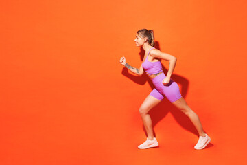 Fototapeta na wymiar Full body sideways young fitness trainer instructor woman sportsman wears top shorts purple clothes train in home gym going to run isolated on plain orange background. Workout sport fit abs concept.