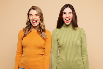 Young fun smiling happy friends two women wear orange green shirt casual clothes together look camera blink eye wink isolated on plain pastel light beige background studio portrait. Lifestyle concept.