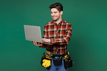 Young employee laborer handyman IT man wear red shirt hold use work on laptop pc computer isolated on plain green background. Instruments accessories for renovation apartment room Repair home concept