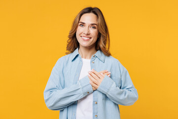 Young smiling happy grateful fun woman she wears blue shirt white t-shirt casual clothes put folded hands on heart look camera isolated on plain yellow background studio portrait. Lifestyle concept.