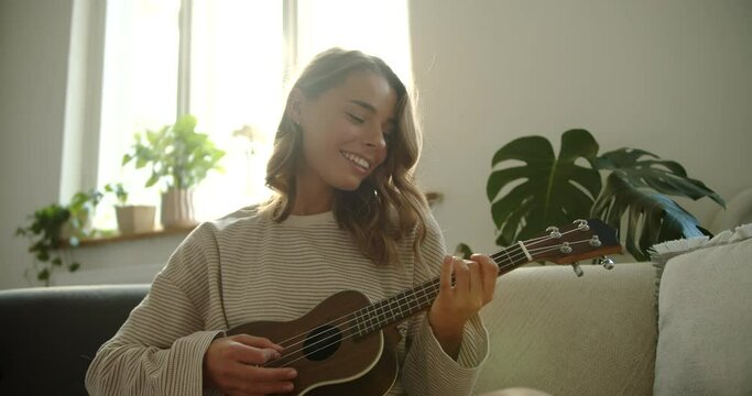 Woman on couch playing ukulele, a plucked string instrument