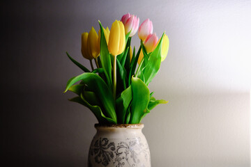 tulips in an old vintage vase against a white wall yellow and pink flowers in a vase on a table