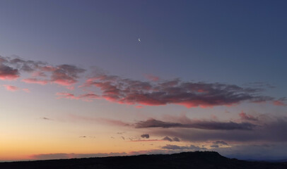 La Luna all’alba resta ancora nel cielo sopra le nuvole rosa sulla colline mentre il sole sorge dal mare