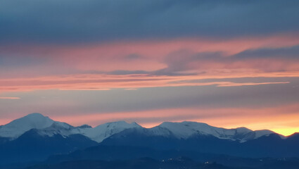 Tramonto arancio sopra le cime dei monti innevate