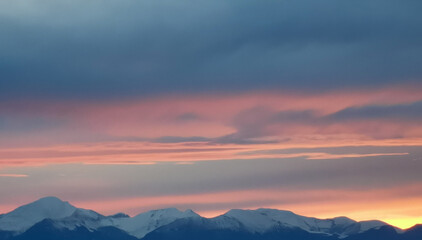 Obraz premium Tramonto arancio sopra le cime dei monti innevate