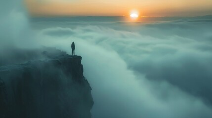 A lone person stands on a cliff edge above the clouds as the sun rises.