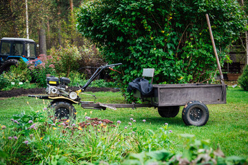 A mini hand-held tillerblock with a cart trolley for working in the garden and on the farm against...