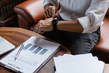 Hands of businessman checking time on smartwatch while working about financial document of business
