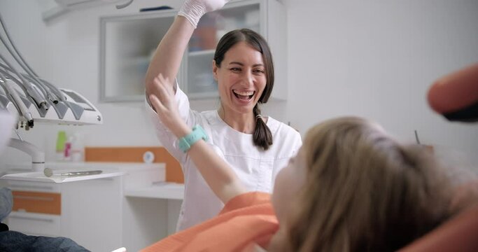 A heartwarming video of a female dentist interacting with young patients in a cheerful dental office setting, giving high fives and smiling while talking to them in a dental chair