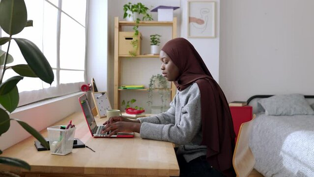 Young african student woman in muslim headscarf using laptop in her bedroom. Gen Z young african woman learning or studying online in her room. Education and technology concept. 4k footage