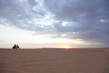 ouple looking at the sunset over the sand dunes at the Sahara desert - 754850520