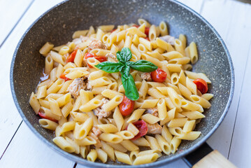 Italian pasta with swordfish, cherry tomatoes, oil and basil in a pan on a table Selective focue