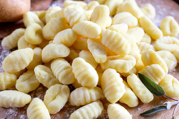 Uncooked homemade potato gnocchi on cutting board over wooden table with flour. See series.