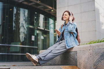 Young Caucasian happy cheerful woman in headphones listening to music using smartphone and internet - 754865722