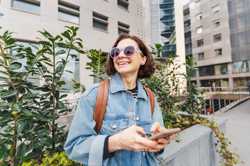 Young European woman in sunglasses standing against the background of a modern residential area on a spring day - 754866317