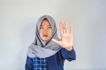 Young asian woman wearing blue shirt with gray hijab makes hand refusal gesture, saying no violence, harassment, abortion, showing palm, declaring prohibition, rejection, fighting against discriminati