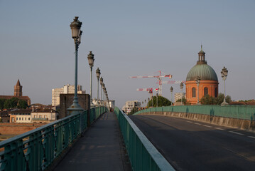 Pont Saint-Pierre Bridge in Toulouse, France. A serene early morning or evening scene of an empty bridge with ornate lamp posts leading towards a dome-capped building. In the background, construction.