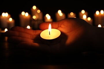 Woman with burning candle in darkness, closeup. Memory day