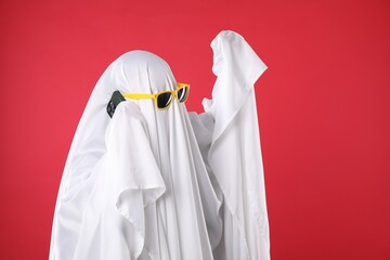 Person in ghost costume and sunglasses talking on smartphone against red background