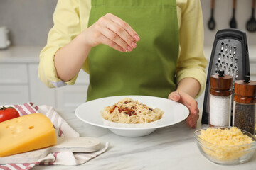 Woman pouring grated cheese onto delicious pasta at white marble table in kitchen, closeup