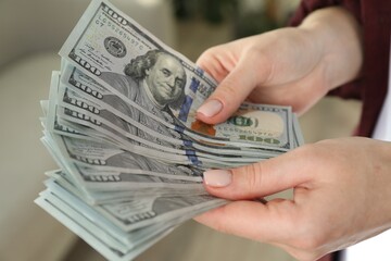 Money exchange. Woman counting dollar banknotes on blurred background, closeup