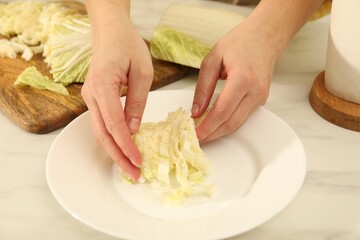 Woman putting cut Chinese cabbage into plate at white kitchen table, closeup
