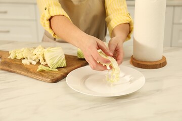 Woman putting cut Chinese cabbage into plate at white kitchen table, closeup
