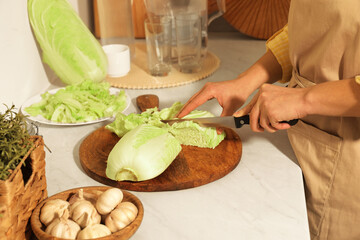 Woman cutting fresh chinese cabbage at kitchen table, closeup