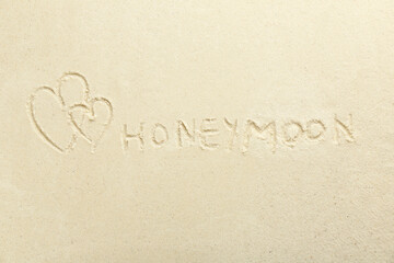 Word Honeymoon written on sand and hearts, top view