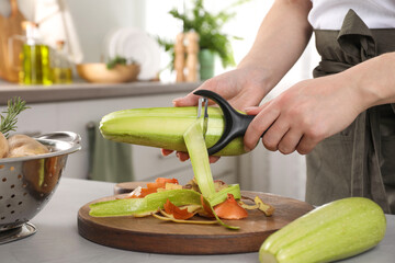 Woman peeling fresh zucchini at light table indoors, closeup