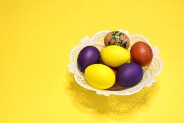yellow, purple and brown easter eggs in white basket on yellow background copy space