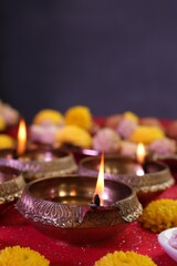 Diwali celebration. Diya lamps and chrysanthemum flowers on shiny red table, closeup