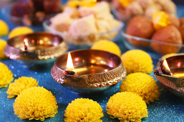 Obraz na płótnie Canvas Diwali celebration. Diya lamps and chrysanthemum flowers on shiny light blue table, closeup