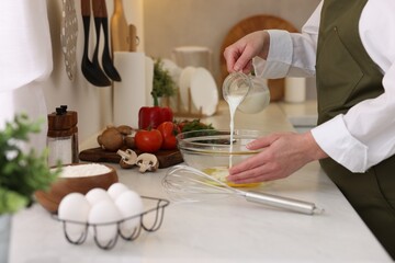 Woman pouring milk into bowl at light table indoors, closeup